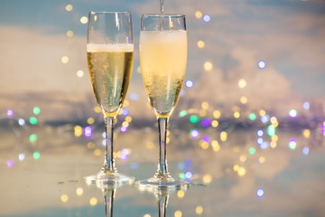 Serving as a luxurious sparkling champagne in two glass cups against a background illuminated by many small lights. Concept of celebration.