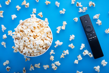 Close-up of remote control and testy warm popcorn viewed from above on blue background. The concept...
