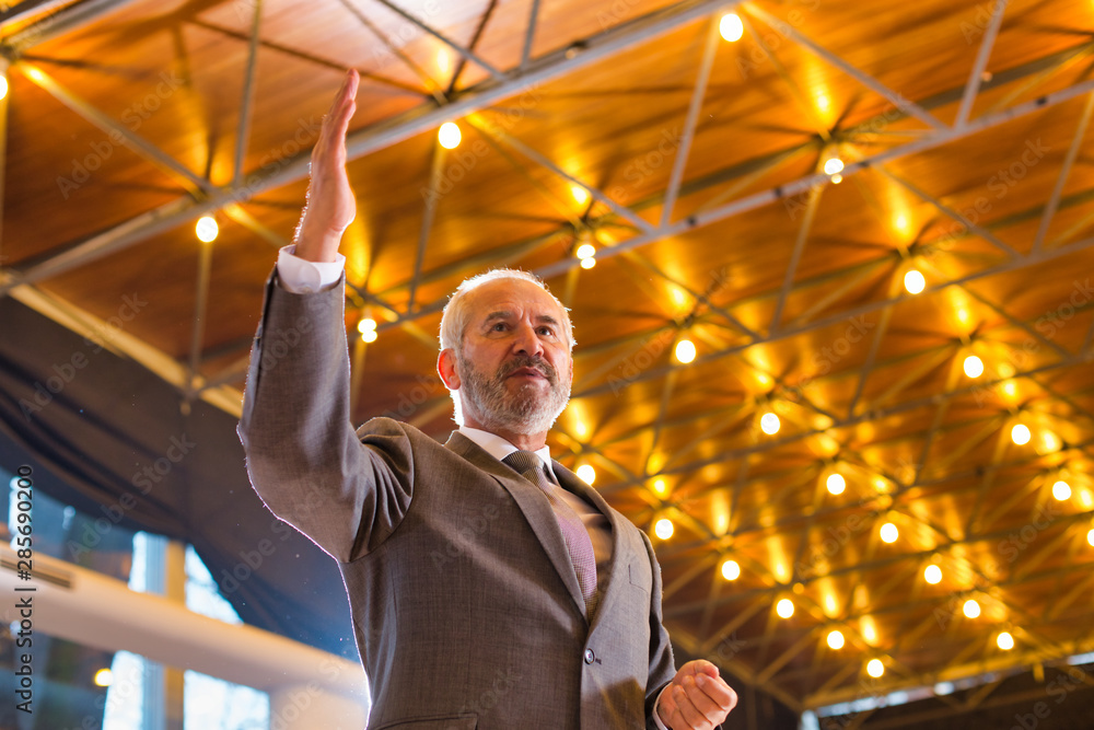 Wall mural Senior businessman in suit gesturing while standing against illuminated roof