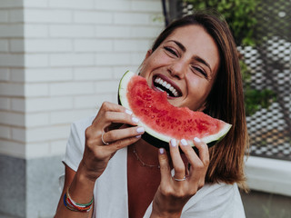 Caucasian woman eating watermelon slices in the garden of her house and sitting on the ground.