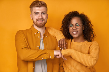 Young diverse couple gives fist bump, agree to bring the plan to life, smile broadly, have mixed race relationships, have good friendly partners, isolated over yellow wall. I agree with your concept