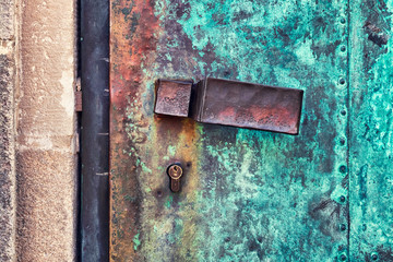 Close-up detailed photo of a worn, used iron doorhandle on a rusty door