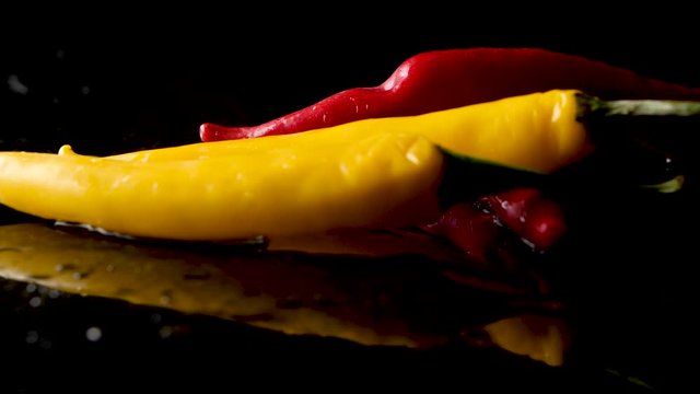 Slow Motion Red And Yellow Chili Peppers Falling On black reflecting surface covered in water