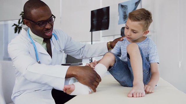 Male doctor inspecting bandage on the leg of little boy.