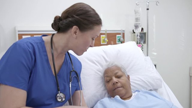 Nurse reviews information on a tablet with a patient in a hospital bed