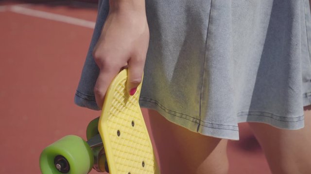Unrecognized girl holds a yellow skete in her hands while standing in sunny weather outdoors.