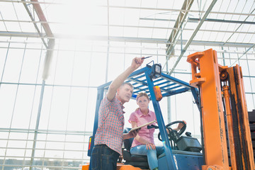 Young woman driving forklift while senior talking to senior in greenhouse