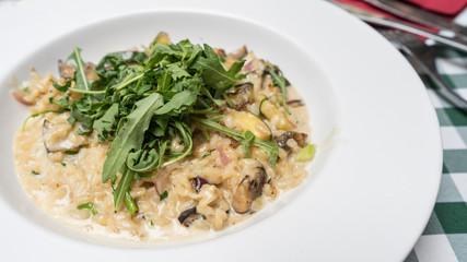Lunch of risotto with mushroom and basil leaves on the top. Square tablecloth and cutlery.