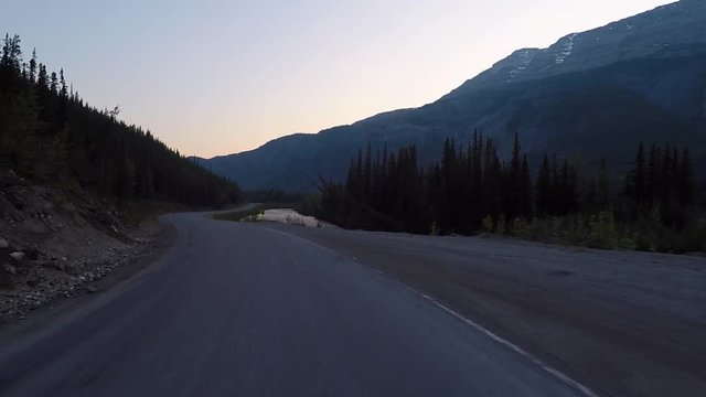 Driving alongside the Alaska highway during sunset next to river.