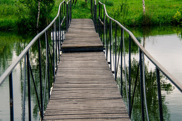Fototapeta premium A narrow wooden bridge with metal railings leads across the river to the shore