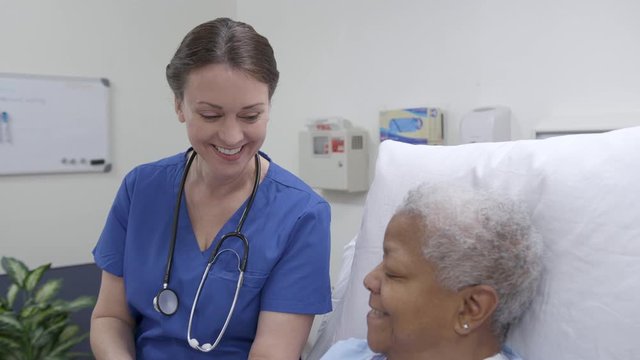 Nurse with a tablet reviews information with patient in a hospital bed