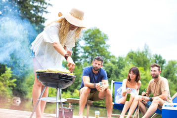 Woman preparing food in barbecue grill with friends on pier