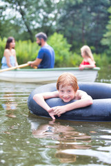 Portrait of smiling boy floating with inflatable ring in lake against family