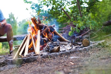 Man drinking beer while sitting on bench at park with bonfire
