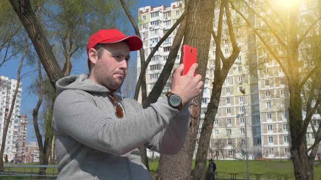 Man makes photos on mobile phone, take a pictures. Funny guy in red cap makes selfie on smartphone