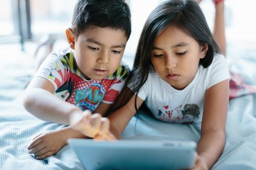 Two siblings lying on bed using a tablet