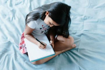 Young girl sitting on the bed writing on a notebook