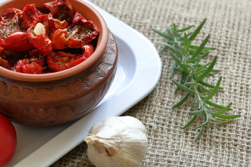 Sun-dried tomatoes with spices and garlic in a clay pot. Near rosemary, tomatoes and garlic.