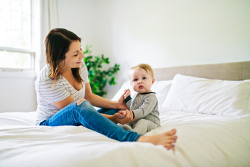 Mother and child on a white bed playing in sunny bedroom