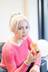 Happy charming blonde young woman eating small cakes
