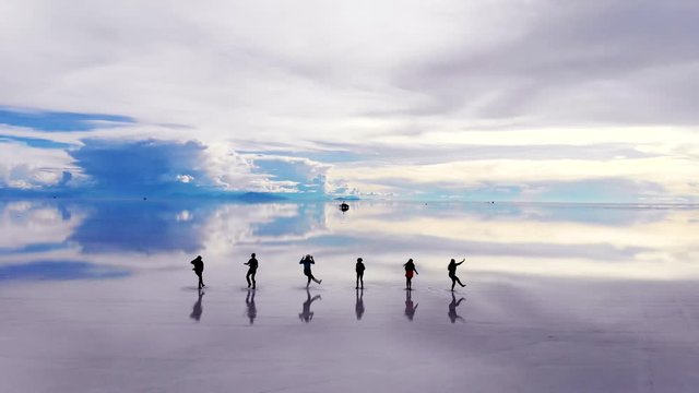 Aerial of silhouetted people dancing on the Uyuni salt flats lake with perfect reflections in Bolivia.