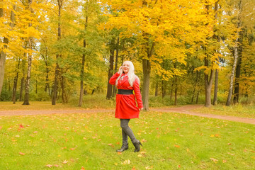 young pretty plus size caucasian blonde woman in red wool coat walks in autumn park