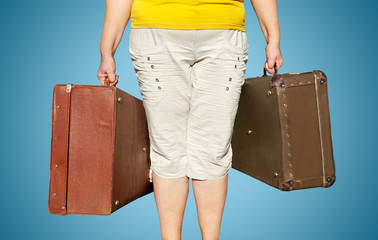 A woman in a yellow T-shirt stands with suitcases in her hands.