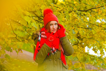 young pretty plus size caucasian woman in red hat with pompom and knitted gloves walks in autumn park
