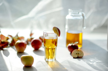 Apple juice in a tall glass. In the background apples and a decanter with a drink. Light...
