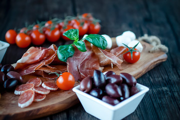 Prosciutto, bread, olives, walnut, mozzarella, salami, basil and cherry tomatoes on  brown wooden...