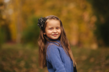 Portrait of little girl in the autumn park. Girl model poses to photographer. Happy child