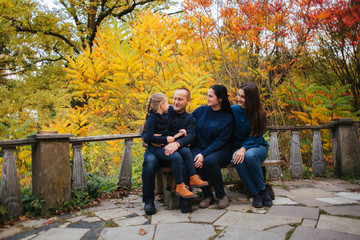 Portrait of happy family sitting on the bench in the forest. Autumn weather and colorful trees