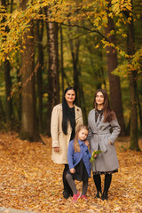 Naklejka na ściany i meble Mom and two daughter have fun in ther park. Youngest daughter collect leaves and smile. Happy family walking in the forest