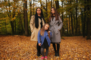 Mom and two daughter have fun in ther park. Youngest daughter collect leaves and smile. Happy family walking in the forest