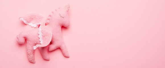 Close-up of felt toy unicorn from baby mobile on pink background with copy space. Preparation for the birth of a child. Baby shower.