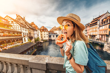 Happy asian girl tourist eating delicious pretzel while travelling in Europe. Tourism and food concept