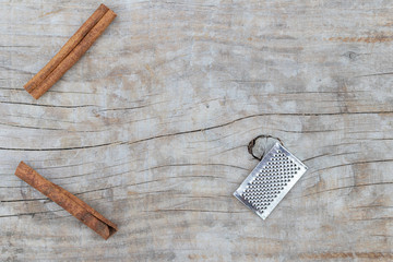 Two cinnamon sticks and mini grater on a wooden background