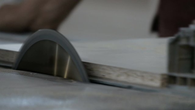 Close-up. A man on a machine with a circular saw cuts a white chipboard. Furniture manufacture. Workshop for sawing parts from sheet materials with an original sound.