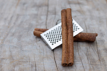 Two cinnamon sticks and mini grater on a wooden background