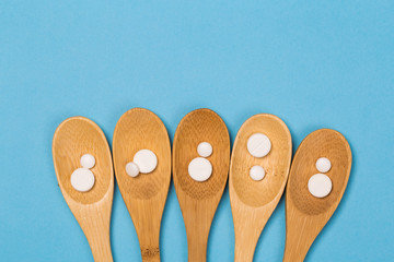 Assorted pharmaceutical medicine pills, tablets and capsules on wooden spoon. blue background