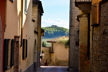 Narrow street and facades with house on a hill in the background, in Piamonte, Italy