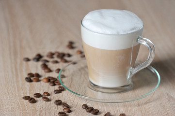Cappuccino in a transparent cup on a light surface. Coffee beans on the surface of the table. Close-up. 