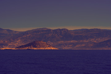 Toned background made of seascape with rocky island, mountains in mist