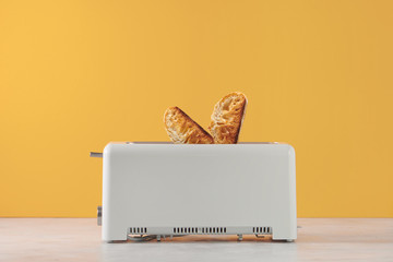 Roasted toast bread popping up of toaster with yellow wall