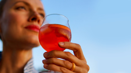 Summer cocktails. Cheers, woman holding cocktail, aperol in the hand outdoors over blue sky, focus...