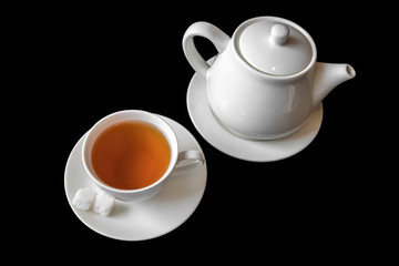 Filled Cup of tea and kettle on black background.