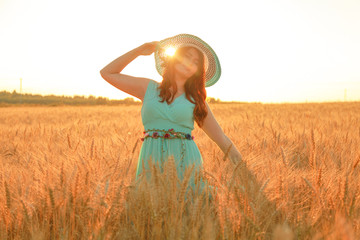 girl in blue dress walking in golden ripe wheat field at sunset