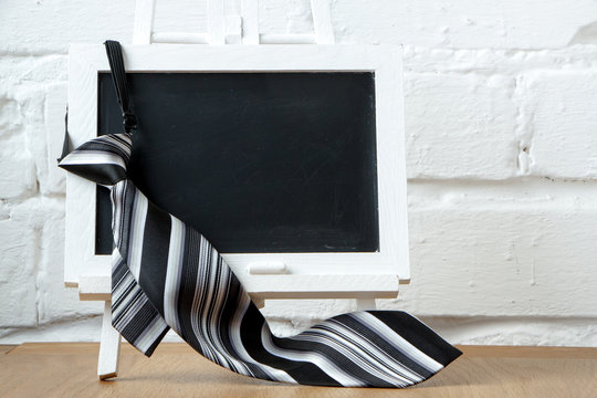 Close-up of a miniature chalk board and striped tie against a white brick wall, selective focus