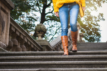 Fashion woman wearing jeans, leather boot and knitted sweater. Woman walking down ancient staircase