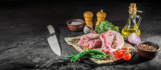 Raw steak with fresh herbs and oil on black background, top view